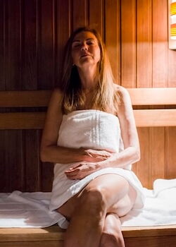 Eine Frau sitzt in der Sauna mit einem Handtuch und genießt die Wärme.