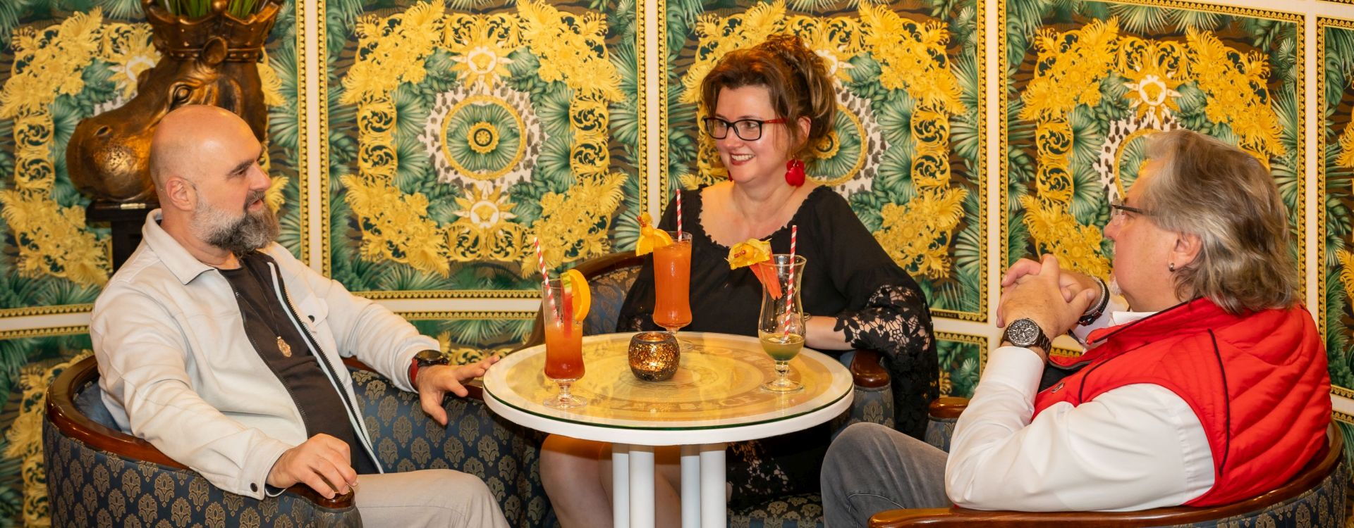 Zwei Herren und eine Damen genießen leckere bunte Cocktails in der Hotelbar.