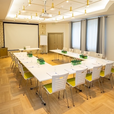 Ein heller Konferenzraum mit Tischen in U-Form und einer großen Leinwand.