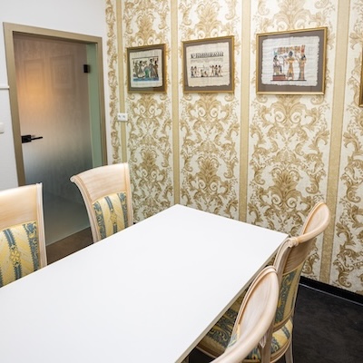 Ein kleiner heller Raum mit einem Tisch und vier Stühlen an einer gemusterten Wand.